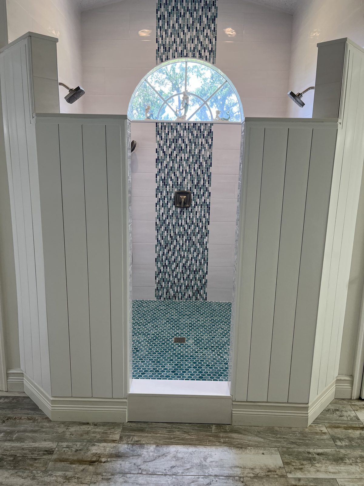 Walk-in shower with arched glass mosaic accent column, dual shower heads, shiplap surround, and turquoise penny tile floor