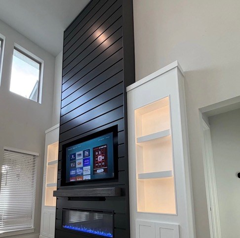 Two-story black diagonal shiplap TV and fireplace accent wall with lit niche shelving by Jeff Handyman