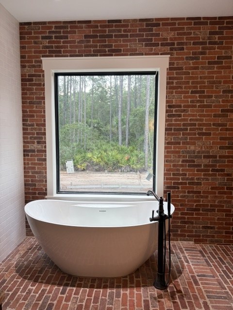 Freestanding soaking tub on a brick floor in front of a brick accent wall and picture window by Jeff Handyman