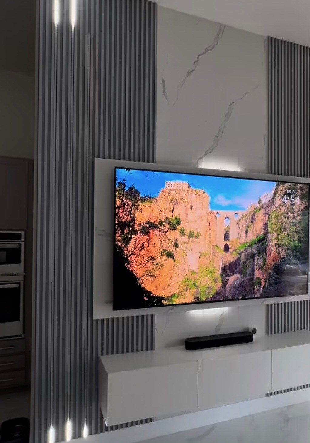TV accent wall with vertical gray fluted slat panels and marble center, floating media console, and LED back lighting