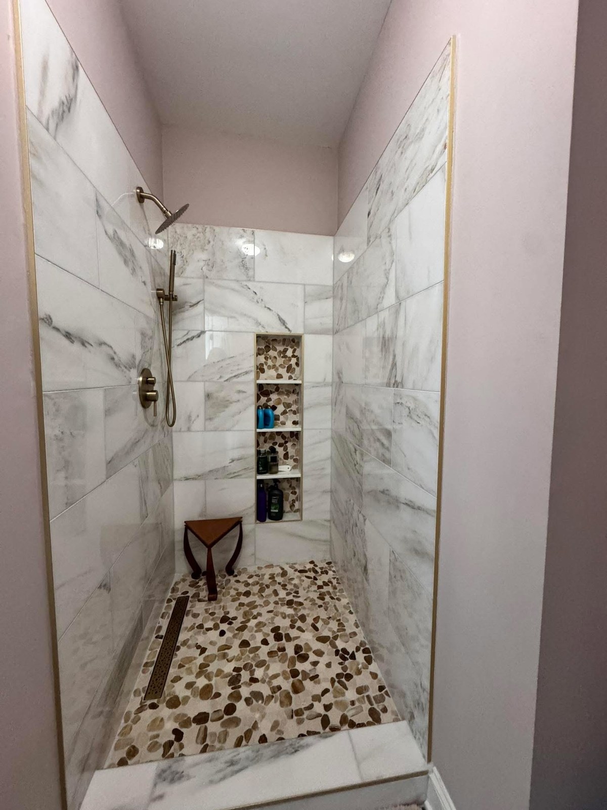 Walk-in shower with black and white pebble mosaic tile floor and white marble walls