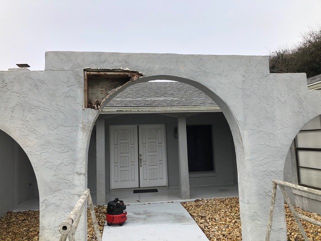 Damaged stucco section above an arched doorway before Jeff Handyman repaired it