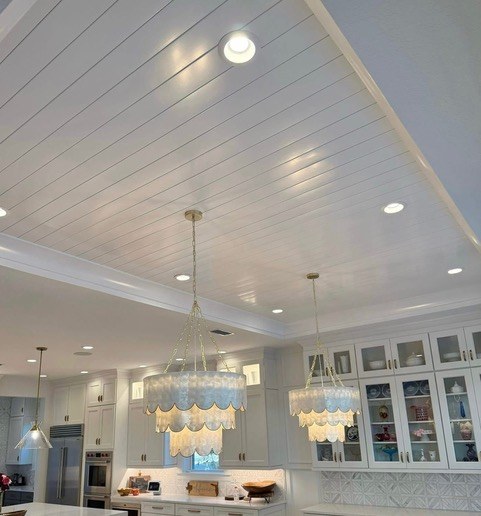 White vinyl plank ceiling install with crystal chandeliers in an open-plan kitchen by Jeff Handyman